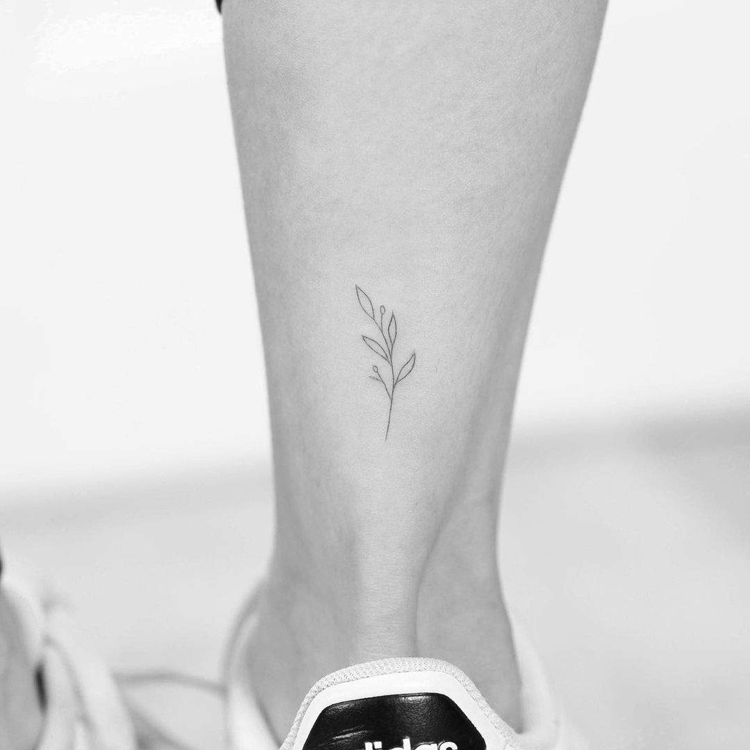 Rama de trazo fino tatuada en la pierna