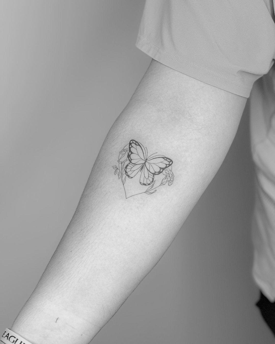 Una mariposa unida a un corazón y dos flores en un mismo tattoo